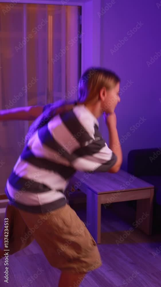 Purple lighting highlighting blond girl dancing dynamically, wearing striped top and cargo shorts, practicing contemporary choreography in home living space Purple lighting highlighting blond girl dancing dynamically, wearing striped top and cargo shorts, practicing contemporary choreography in home living space