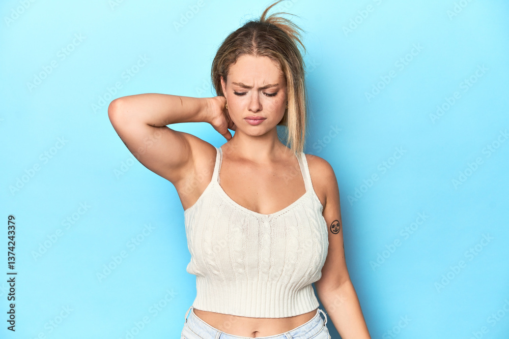 Naklejka premium Blonde young woman in white top on blue background suffering neck pain due to sedentary lifestyle.