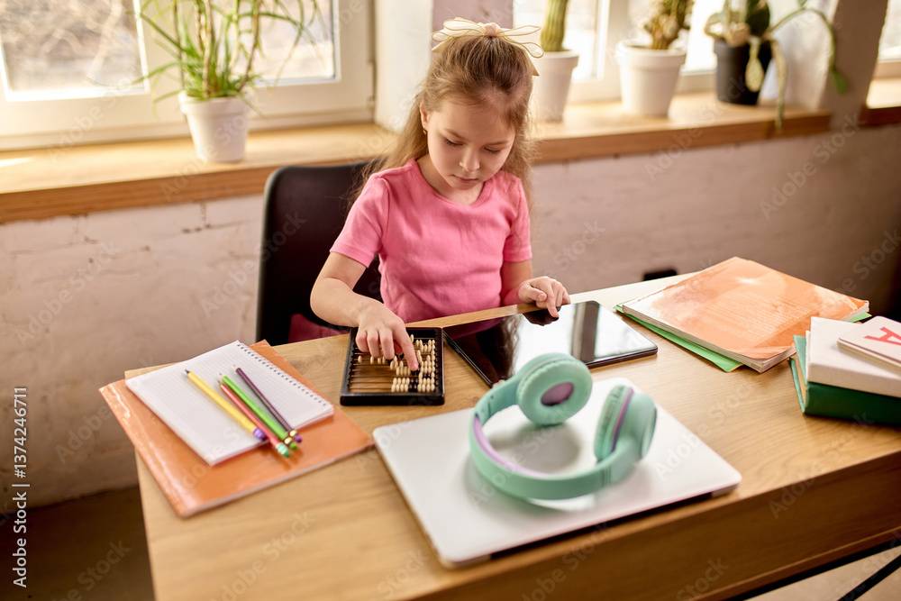 Girl using wooden abacus while studying at desk with digital tablet and school supplies in warm daylight interior. Math. Concept of childhood, online education, remote studying Girl using wooden abacus while studying at desk with digital tablet and school supplies in warm daylight interior. Math. Concept of childhood, online education, remote studying