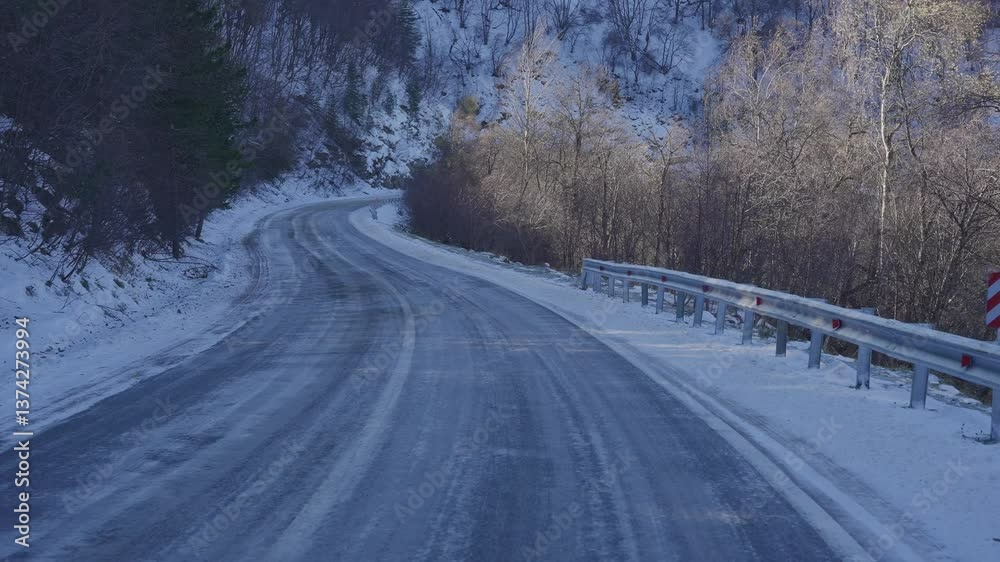 Snow-covered mountain road with icy patches and guardrail Snow-covered mountain road with icy patches and guardrail