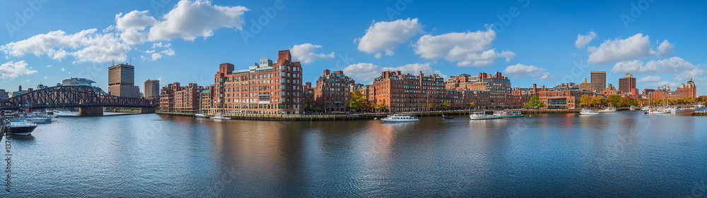 Fototapeta premium Traditional city buildings with red brick facades reflecting in the river water under a sunny blue sky. A warm and welcoming urban setting for stock and editorial use. 