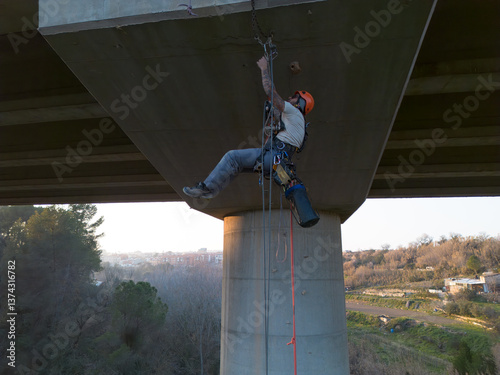 Rope access technician inspecting underside of concrete bridge structure