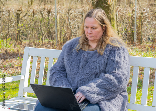 Obraz na płótnie Frau in einer Kaninchenfell Jacke arbeitet im Garten mit einem Notebook im Homeoffice
w salonie