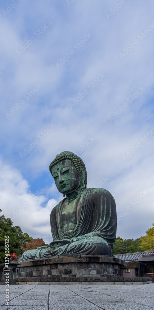 Fototapeta premium Vertical composition of the Great Buddha in Kamakura Japan captured from below showcasing the grand scale of the bronze statue with a dominant sky