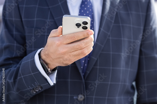 Businessman dressed in stylish suit. He holds smartphone in one hand. using phone in work tasks. checking social networks or watching news. using modern technologies