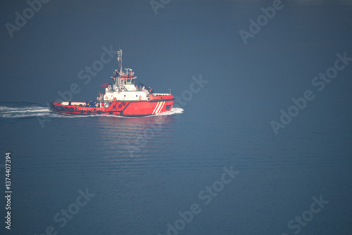 Fototapeta Naklejka Na Ścianę i Meble -  Red tugboat passing through the Bosphorus. Tugboat in blue sea or ocean. Top view. Copy space, blank, emtpy. 