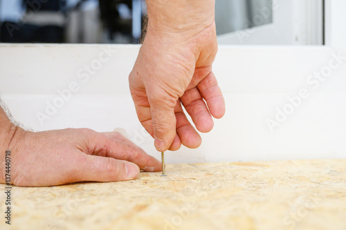 Fotografie Male hands screwing screw into wooden surface manually.