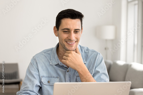 Man sits at desk with laptop working from homeoffice, read emails, responding to messages, researching online, looking up information, planning tasks, enhancing his skills through educational content