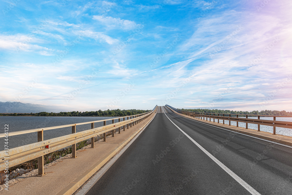 A long, straight bridge stretches over a body of water under a bright blue sky, creating a scenic and peaceful road trip atmosphere.