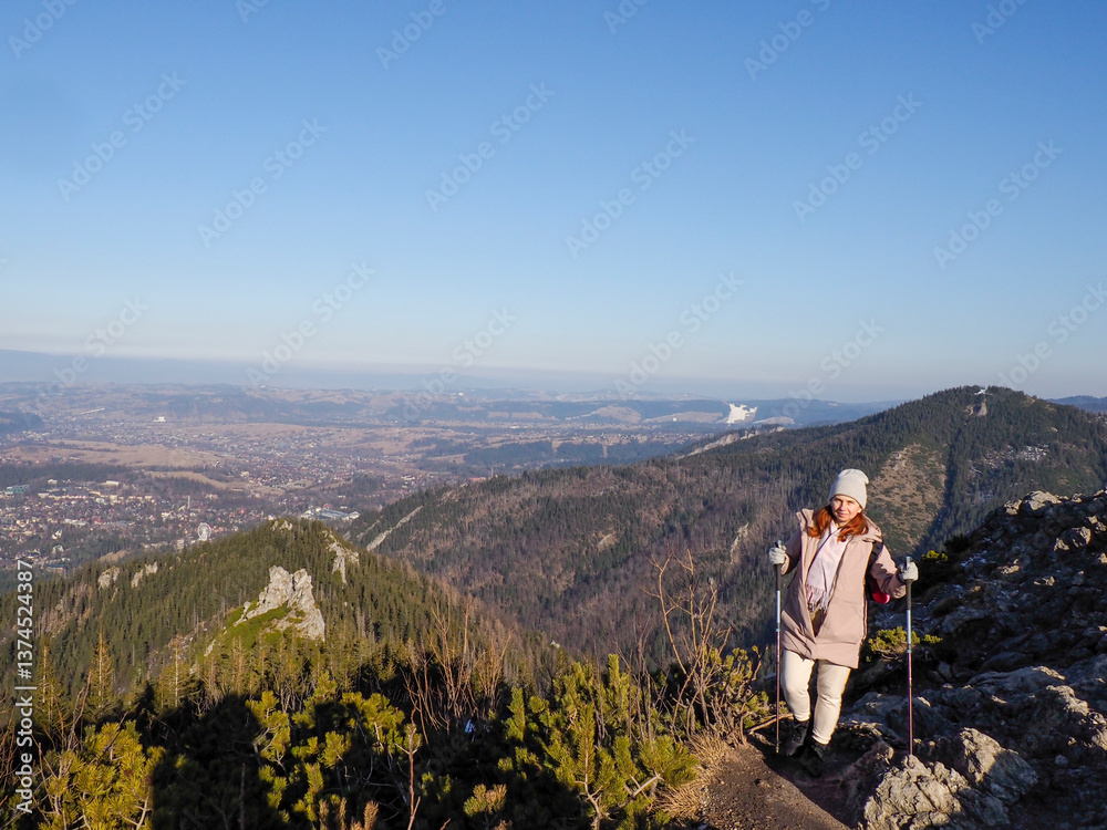 Naklejka premium Solo Traveler in Light Clothing Standing on Rocky Mountain Summit Admiring Breathtaking Valley View in Clear Weather