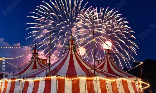 A red and white striped circus tent illuminated by fireworks and string lights at dusk.