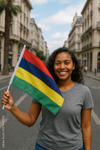 A woman smiles brightly while holding the Mauritian flag in a bustling city street. The surroundings feature beautiful architecture under a clear sky, enhancing the joyful atmosphere