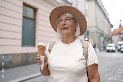 Obraz na płótnie 60s senior woman walking leisurely down a city street with a cone of ice cream, enjoying a moment of calm and happiness under the sun. A perfect blend of relaxation and indulgence. w salonie