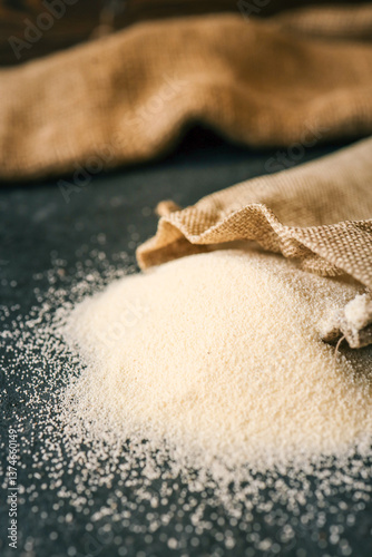 Spilled semolina on a dark surface from a rustic burlap sack. Minimalist food background with focus on texture and natural tone