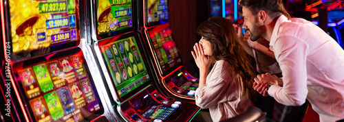 Obraz na płótnie Excited Couple Gambling on Slot Machines at a Colorful Casino w salonie