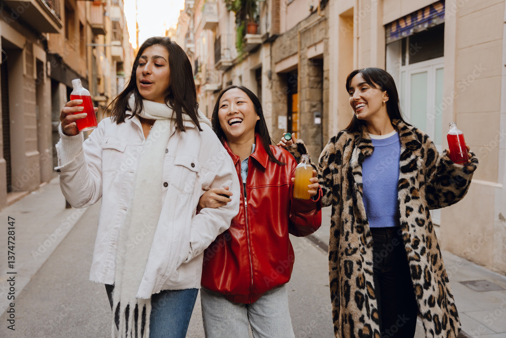 Obraz premium Group of three female friends walking and laughing while talking and holding bottles, outdoors, at a girls' party