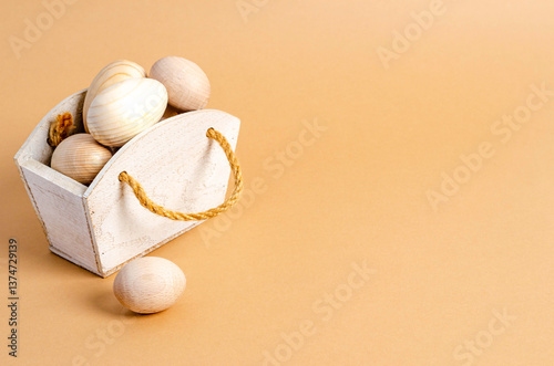 Wooden Easter eggs in a wooden basket on a beige background with text space.