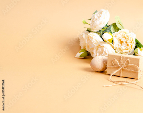 Easter wooden egg, gift box, bouquet of delicate flowers on beige background with text space.