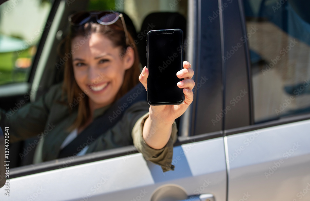 Smiling woman shows smartphone from car window in bright sunlight Smiling woman shows smartphone from car window in bright sunlight