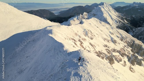 An aerial view of three mountaineers ascending a snow-covered peak, highlighting their journey and the breathtaking landscape.