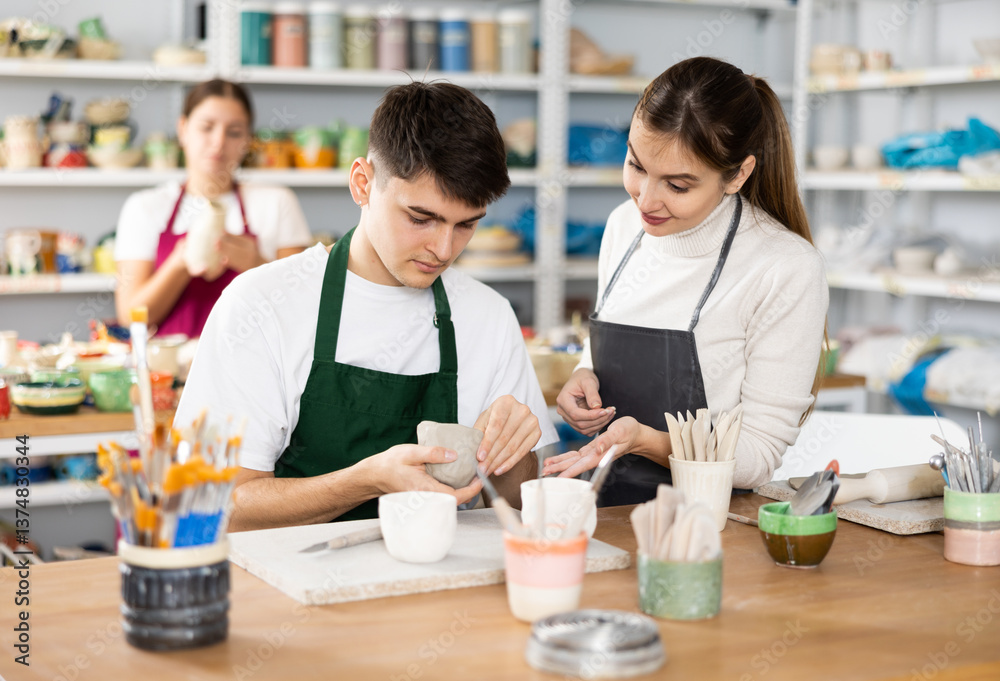 Fototapeta premium Young woman and young man sculpting ceramic product in workshop