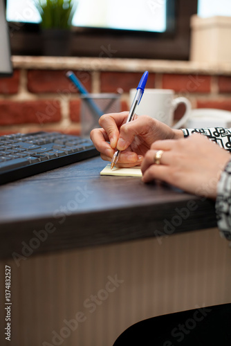Obraz na płótnie Closeup of business person writing on sticky note on office desk, planning work schedule. Selective focus on hands of female employee using a pen, noting down company strategy ideas on table. w salonie