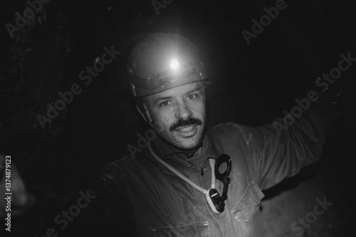 a young caving instructor dressed in a protective suit and helmet shows the route in a cramped gypsum cave
