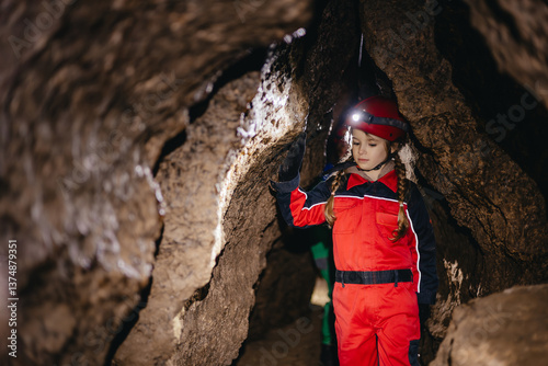 A little schoolgirl in a caving suit in a cramped dark cave enthusiastically follows the tourist route of a gypsum cave explorer