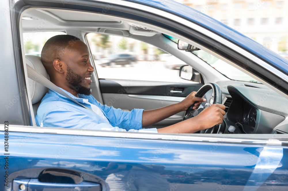 Naklejka premium Happy Driver. Side view profile portrait of cheerful positive African American man sitting in a car on driver's seat. Excited black guy riding in the city, holding hands on steering wheel