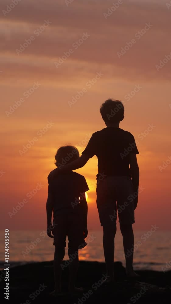 Golden Light Casts A Warm Glow On Silhouetted Brothers Standing By The Shore Golden Light Casts A Warm Glow On Silhouetted Brothers Standing By The Shore