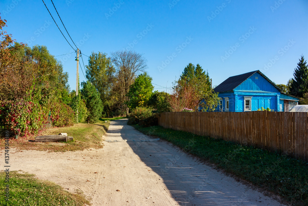 Fototapeta premium Village street with blue house in traditional style. Bolotskoye village, Zhukovsky district, Kaluga region, Russia