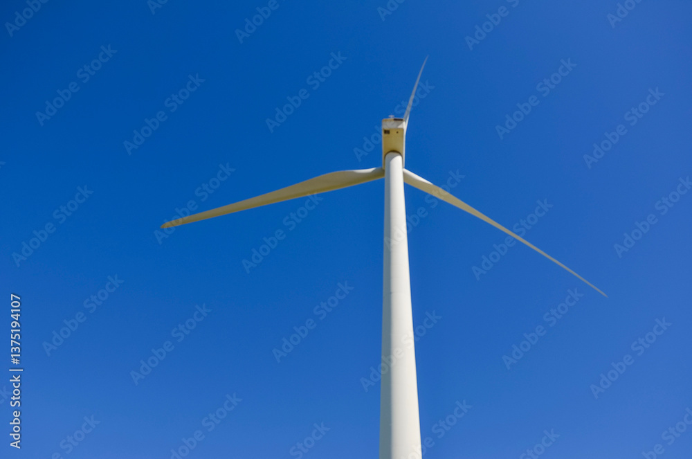 Fototapeta premium Wind turbine generating renewable energy against blue sky