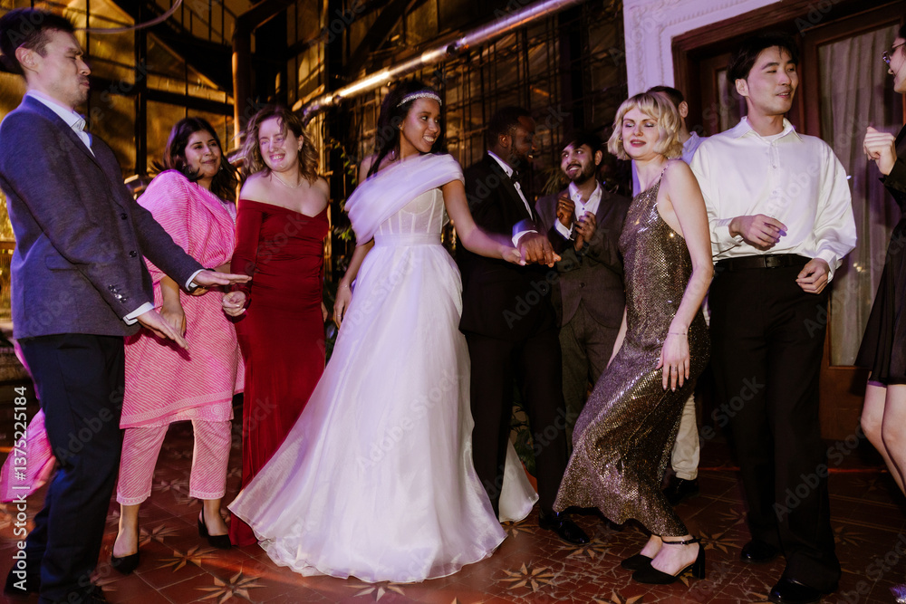 Fototapeta premium A young Black bride in her late 20s, dancing with her young Black groom in the middle of the dance floor, among the wedding guests, in a spacious hall, all having fun and smiling