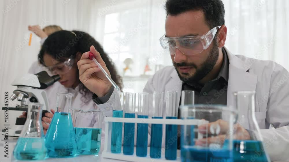 Scientists are researching blue liquid in a lab. young scientist is currently dripping a solution of substance extract into a test tube for research purposes in the science laboratory. Examination. Scientists are researching blue liquid in a lab. young scientist is currently dripping a solution of substance extract into a test tube for research purposes in the science laboratory. Examination.