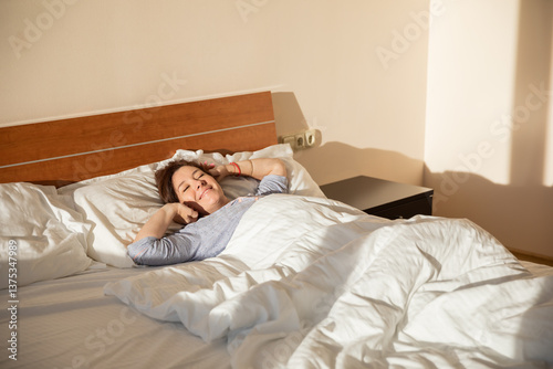 Brunette woman in pajamas woke up on the bed smiling in the morning