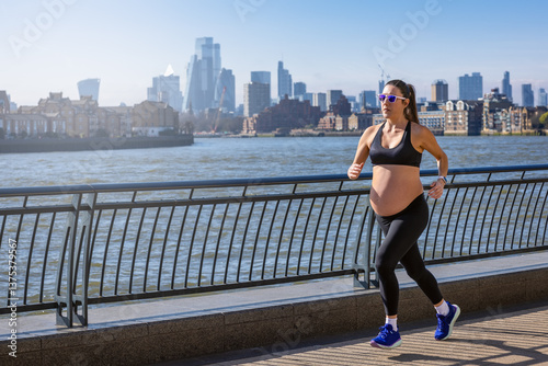 Obraz na płótnie A pregnant woman in sports clothing running for exercise in front of an urban skyline during a sunny day w salonie