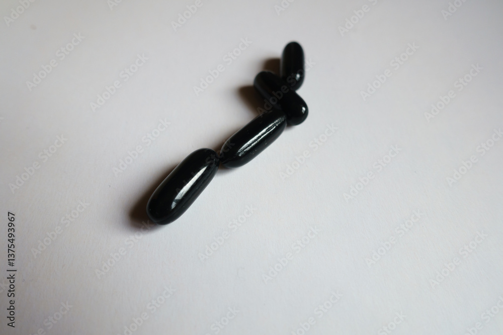 Closeup of four black softgel capsules of activated charcoal