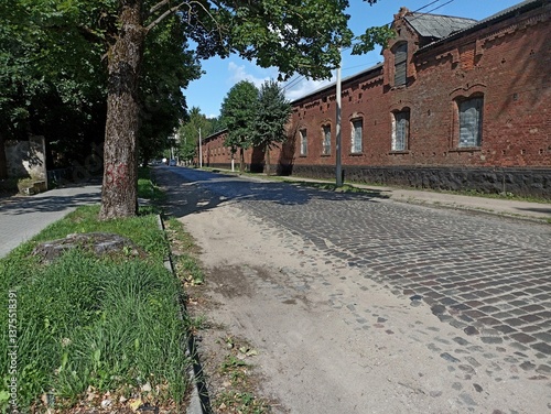 A cobbled street lined with a long brick building with boarded-up windows