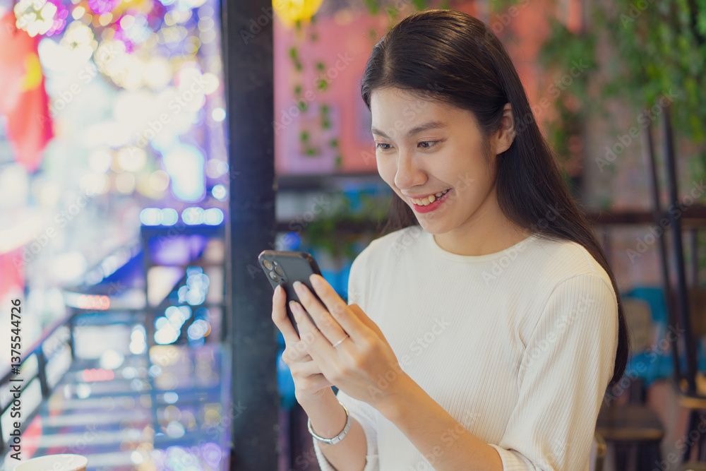 Young Asian woman happily using smartphone in a vibrant cafe during evening hours with colorful lights Young Asian woman happily using smartphone in a vibrant cafe during evening hours with colorful lights