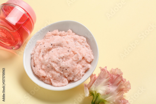 Scrub with cosmetic oil and flower on light yellow background. Body massage concept