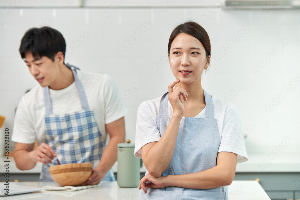 Fototapeta premium The newlyweds are in the kitchen: the husband is cooking while the wife stands nearby waiting for the meal to be ready
