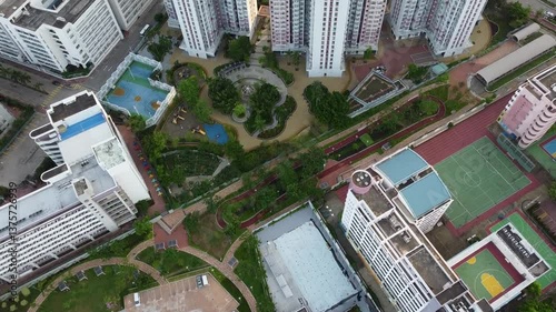Aerial drone view of an urban residential area featuring modern apartment buildings, lush green parks, walking paths, and sports facilities, showcasing a well-planned cityscape.