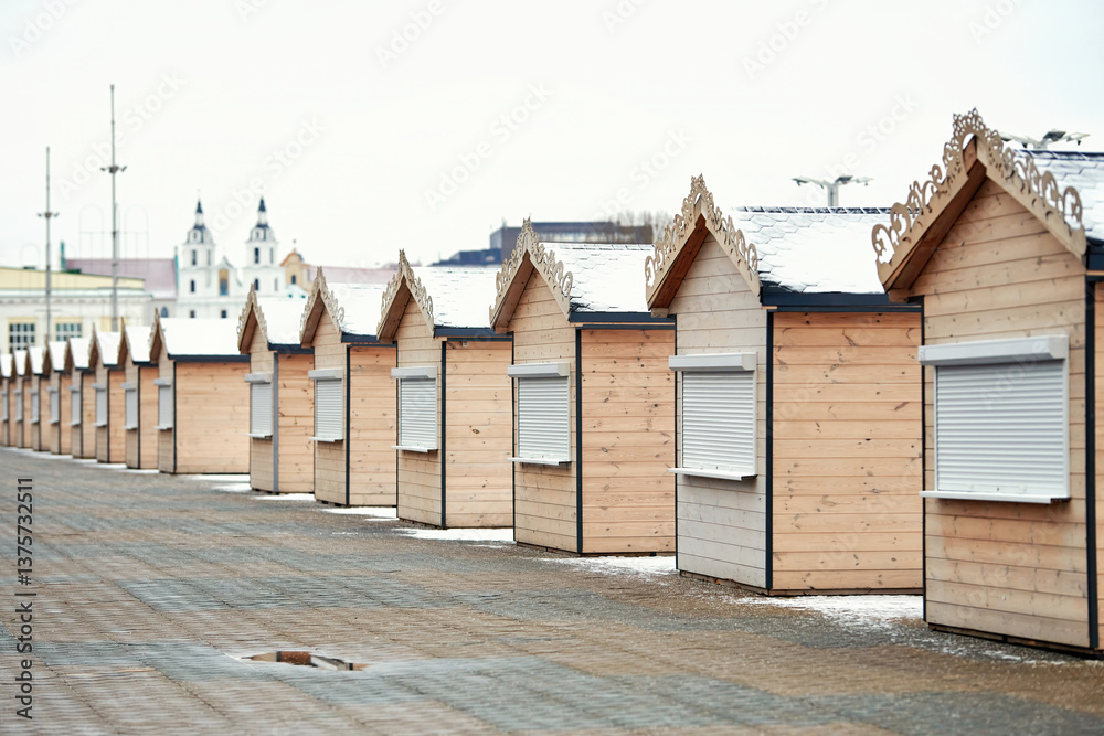 Wooden stalls lined up in an empty outdoor market, prepared for seasonal fair or festive holiday event. Empty winter marketplace with closed wooden kiosks. Market stalls in a neat row, selective focus