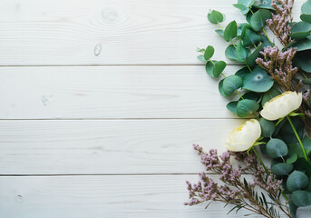 White flowers and eucalyptus leaves creating a border on a white wooden background, providing copy space