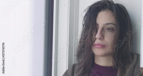 A close-up of a young girl at sunrise after a bad night, tears in her eyes and smeared makeup, standing by the window, feeling very sad.