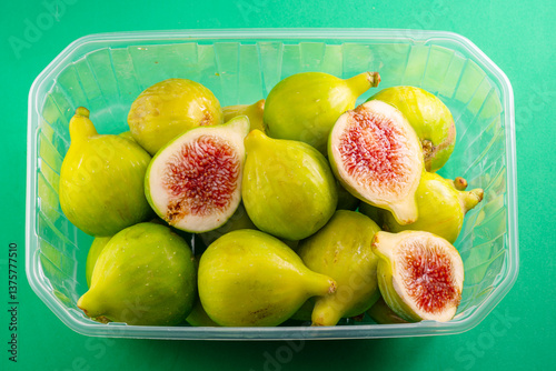 Ripe green fig fruits in plastic box top view isolated on green background. photo