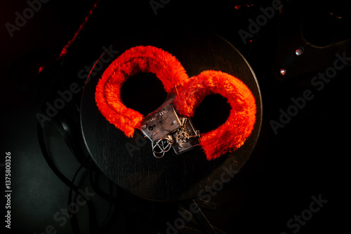 Red handcuffs on a black surface with dramatic lighting showcasing a bold, playful undertone