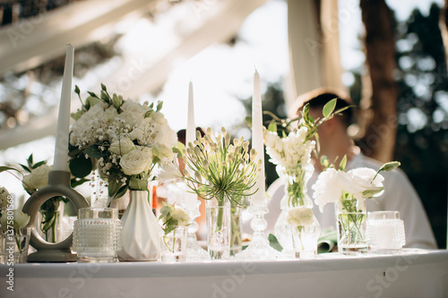 Photos A white floral centerpiece with candles on a white tablecloth in an outdoor even