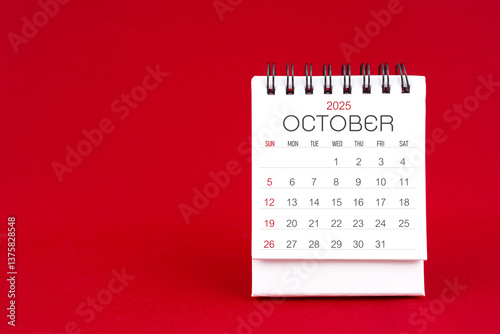 White desk calendar for October 2025 on red background.