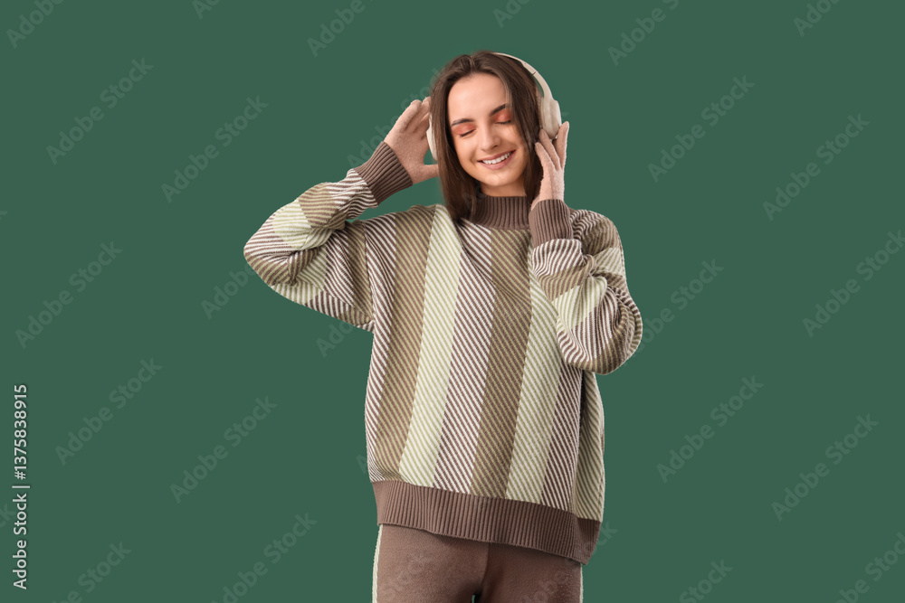 Fototapeta premium Beautiful young woman in stylish sweater and headphones on green background